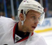 Head view of a hockey player in a white uniform and helmet as he stares intently into the distance.