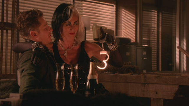Fichier:5x15 David Nolan Cruella d'Enfer sourire coupes verres à pied d'alcool bouteille de champagne idée sexy paire de menottes main.png